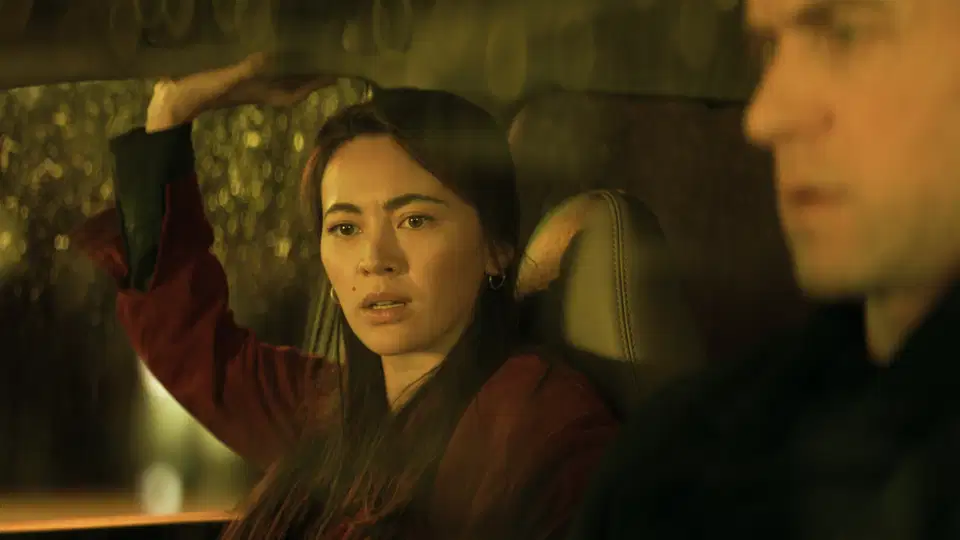 Jessica Henwick sitting in a car looking concerned with one hand raised to the roof, seen alongside Ashley Zukerman in a scene from Silo.