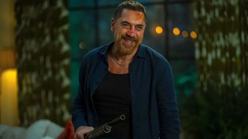 Javier Bardem as Max Cady smiling menacingly with cuts on his face while holding a shotgun in a dark room in Cape Fear.