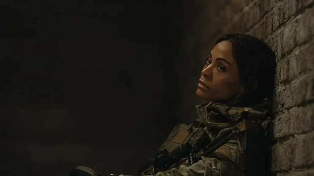 Zoe Saldaña as Joe leaning back against a brick wall in military tactical gear in Paramount+'s Lioness.