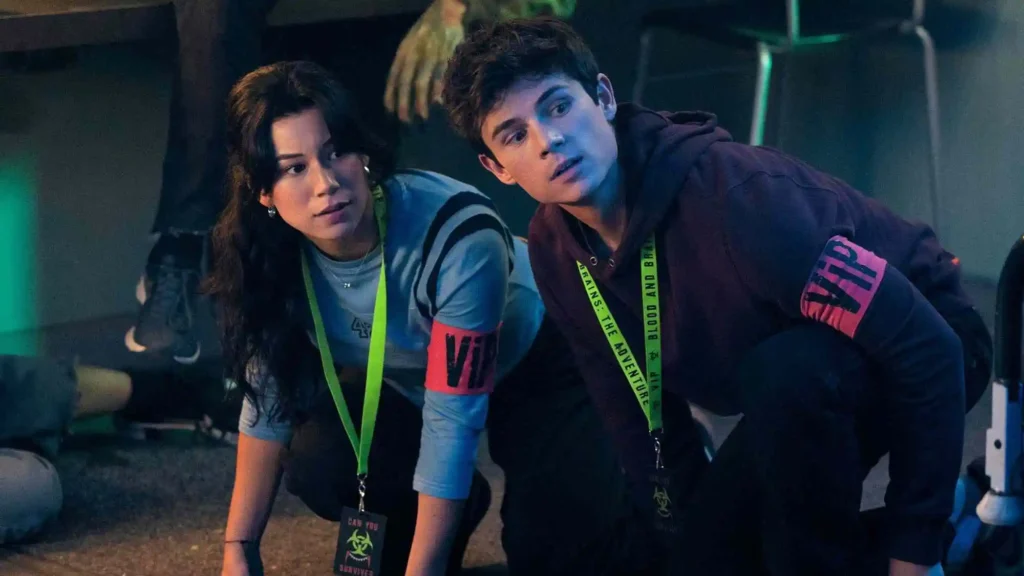 Mya Lowe as Kiley and Ashby Gentry as Alex Walter crouching side-by-side with VIP passes in My Life With the Walter Boys.