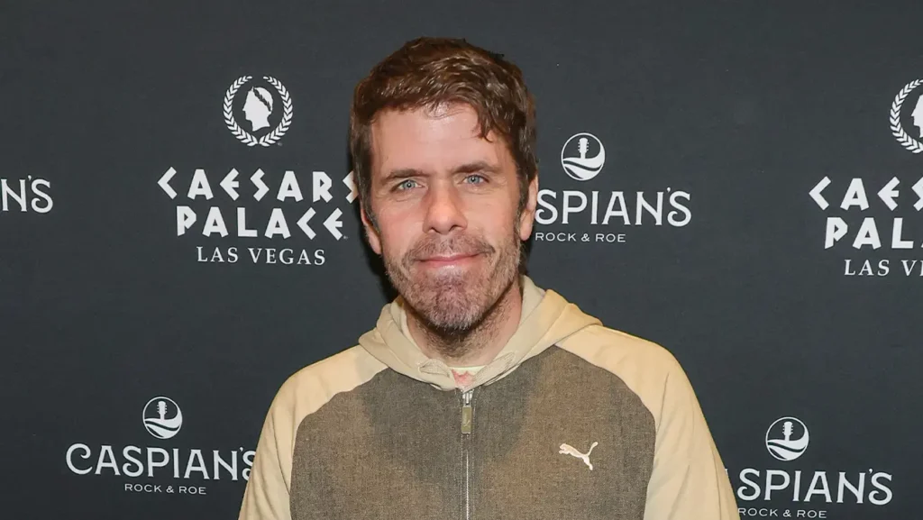 Perez Hilton smiling in front of a Caesars Palace and Caspian's step-and-repeat backdrop at an event.