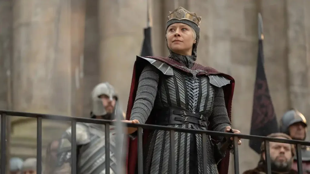 Emma D'Arcy as Queen Rhaenyra Targaryen wearing armor and a crown, looking out over a balcony in House of the Dragon.