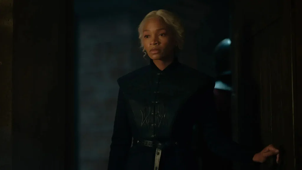 Bethany Antonia as Lady Baela Targaryen wearing a dark embroidered coat and holding a doorway in House of the Dragon.
