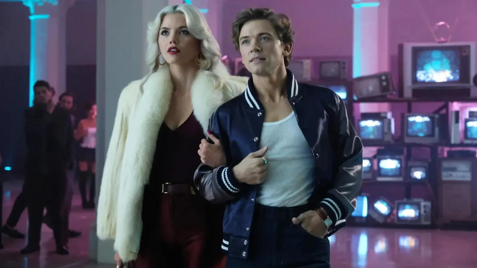 A blonde woman in a white fur coat holding arms with a man in a navy varsity jacket in a scene from The Shards.