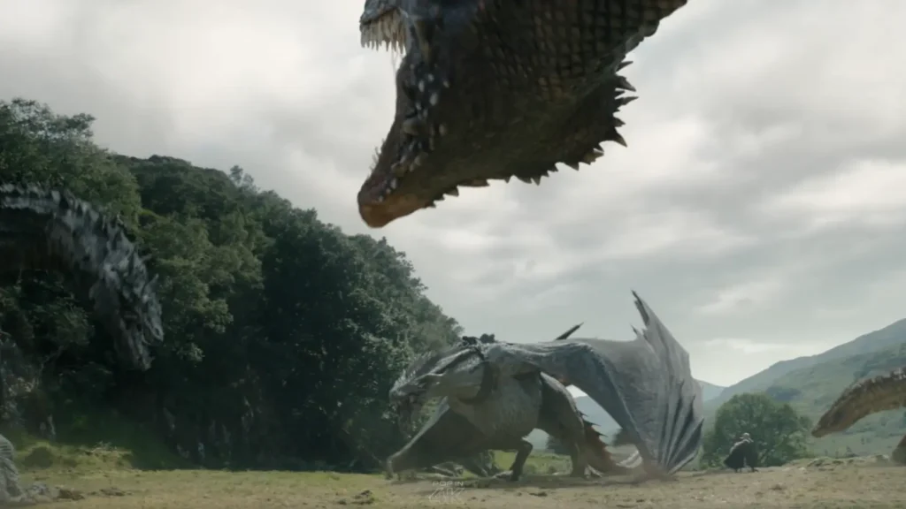 Multiple large dragons gathered on a grassy field against a backdrop of green trees and hills in House of the Dragon.