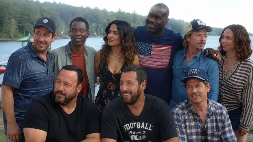 Adam Sandler, Kevin James, Chris Rock, Salma Hayek, Shaquille O'Neal, David Spade, and Maya Rudolph posing together outdoors near a lake.