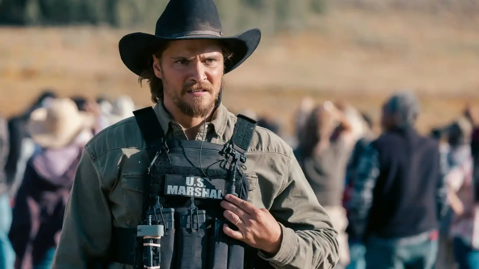 Luke Grimes as Kayce Dutton wearing a dark cowboy hat and a U.S. Marshal tactical vest in Yellowstone.