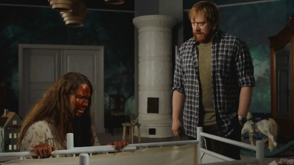 Nightborn: The 2026 Horror Film That Turns Motherhood Into a Nightmare Seidi Haarla covered in blood looking into a crib beside Rupert Grint in a scene from Nightborn.