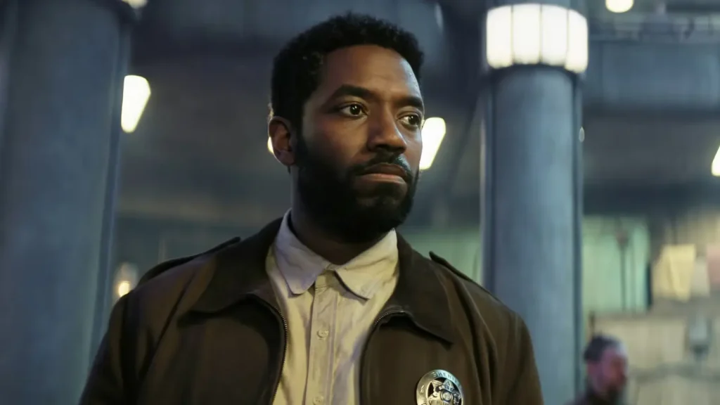 Chinaza Uche wearing a sheriff's badge and dark jacket looking thoughtful in Silo.