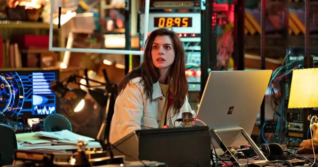 Anne Hathaway sits at a high-tech desk surrounded by monitors and wires, looking up with a wide-eyed, startled expression in Prime Video's Solos.