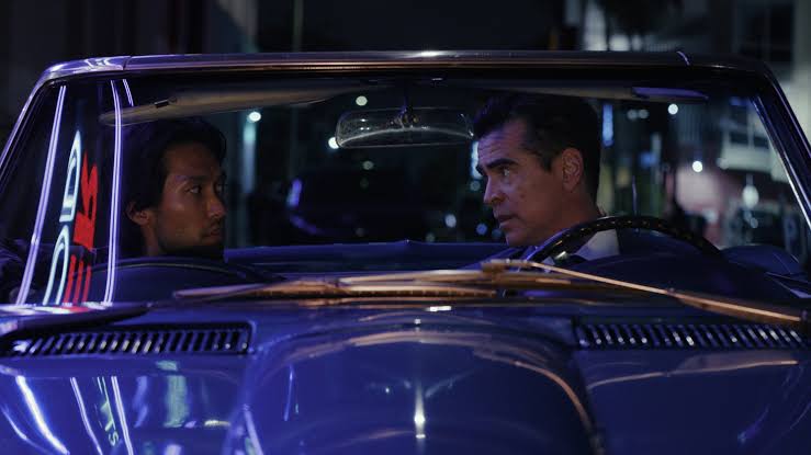 Colin Farrell behind the wheel of a blue classic convertible talking to a male passenger at night in Sugar.